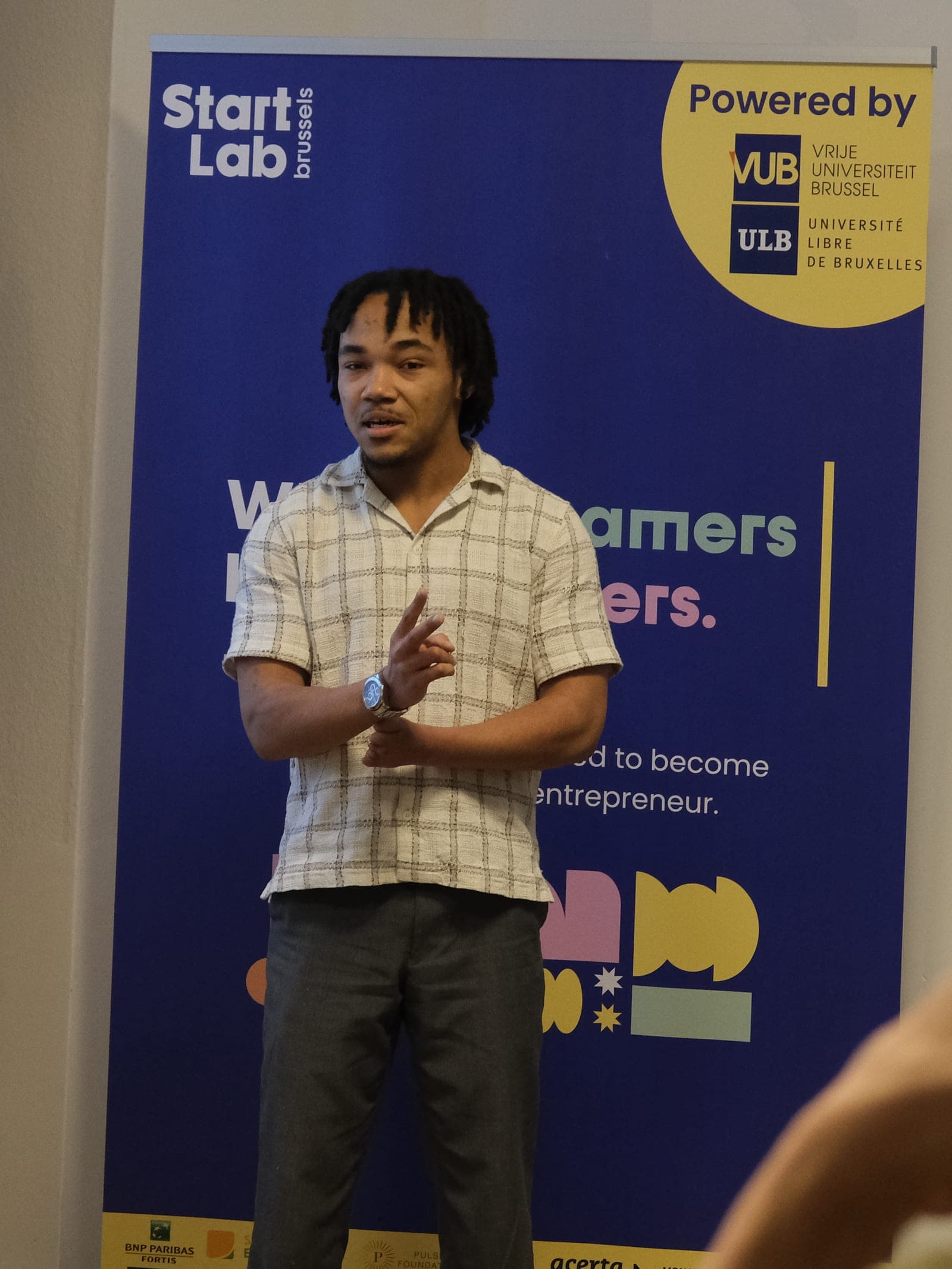 Julius Meto’o Ndongo présentant devant un kakémono StartLab Brussels, VUB et ULB